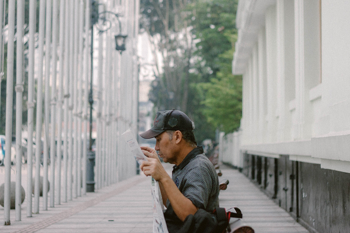 foto tentang seorang pria yang sedang membaca koran di trotoar jalan asia afrika, Bandung